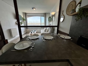 A dining area with a table set for four, a view of the beach, and a window with curtains. - Studio cabin, canal view - 4 guests (Cap d'Agde)
