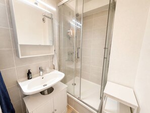 Ein Badezimmer mit einer Duschkabine aus Glas, einem weißen Waschbecken und einem Spiegel darüber.