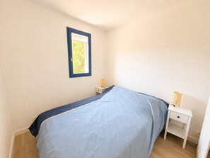 Ein Schlafzimmer mit einem Bett, einem Nachttisch mit Lampe, einem kleinen Beistelltisch und einem Fenster mit Blick ins Grüne.