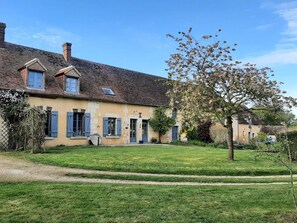 A two-story house with a sloped roof, a small garden, and a tree with pink blossoms. - Welcoming house in the heart of Perche - 8 guests (La Mesnière)