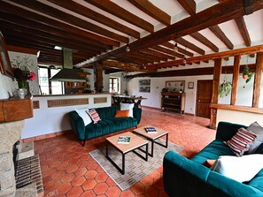 Ein rustikaler Innenraum mit Holzbalkendecke, einem grünen Sofa, einem Holztisch und einer Küchenzeile.