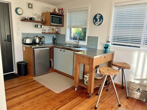 A compact kitchen with a microwave, sink, and wooden cabinets. - Cosy cabin style bach, immersed in native bush, in beautiful Banks Peninsula (Little Akaloa)