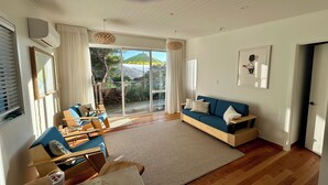 A spacious living room with a blue sofa, wooden furniture, a large window with curtains, and a view of the outdoors.