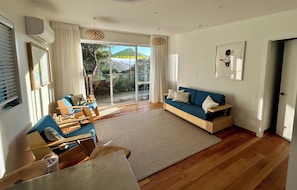 Amplia sala de estar con un sofá azul, muebles de madera, un ventanal con cortinas y vistas al exterior.