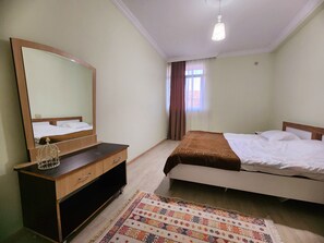 A bedroom with a bed, a dresser, a mirror, a window with curtains, and a ceiling light.