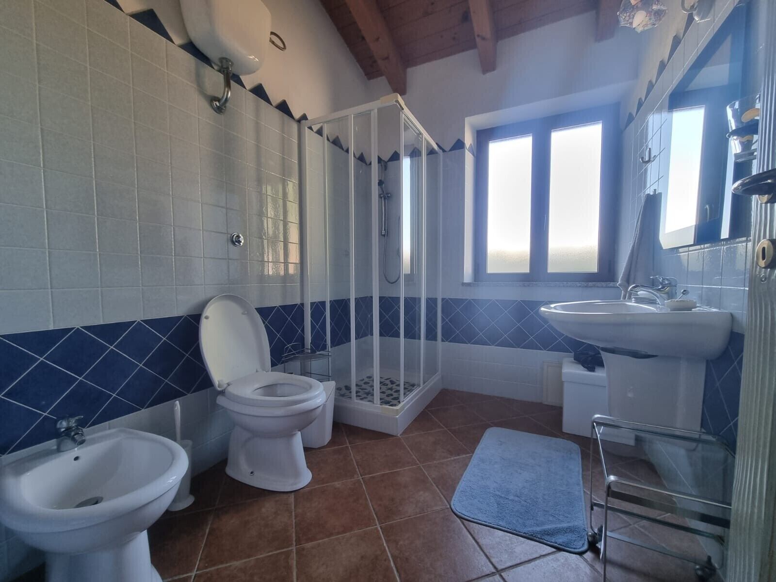 Un bagno con il water, bidet, cabina doccia, lavandino e una finestra.