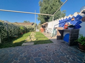 A stone pathway leading to a patio area with a blue-tiled wall, potted plants, and a metal gate.