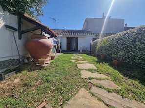 Un sendero de jardín que conduce a un edificio blanco con techo de tejas, rodeado de macetas y una gran maceta de terracota.
