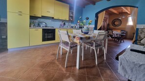 A kitchen with yellow cabinets, a dining area with a table and chairs, and a living area with a couch and a decorative wall. - Casa Lara: Holiday Home with Private Garden and Wi-Fi (Cannigonis)