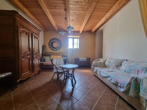 A room with a wooden ceiling, a round table with chairs, a sofa, a cabinet, and a wall clock.