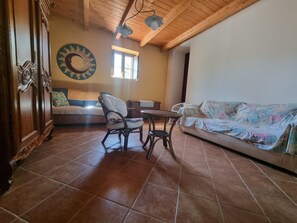 A cozy living room with a wooden ceiling, a round table with chairs, a sofa, and a wall clock.