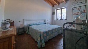 A bedroom with a bed, a desk, a chair, a window, and a ceiling with wooden beams. - Casa Lara: Holiday Home with Private Garden and Wi-Fi (Cannigonis)