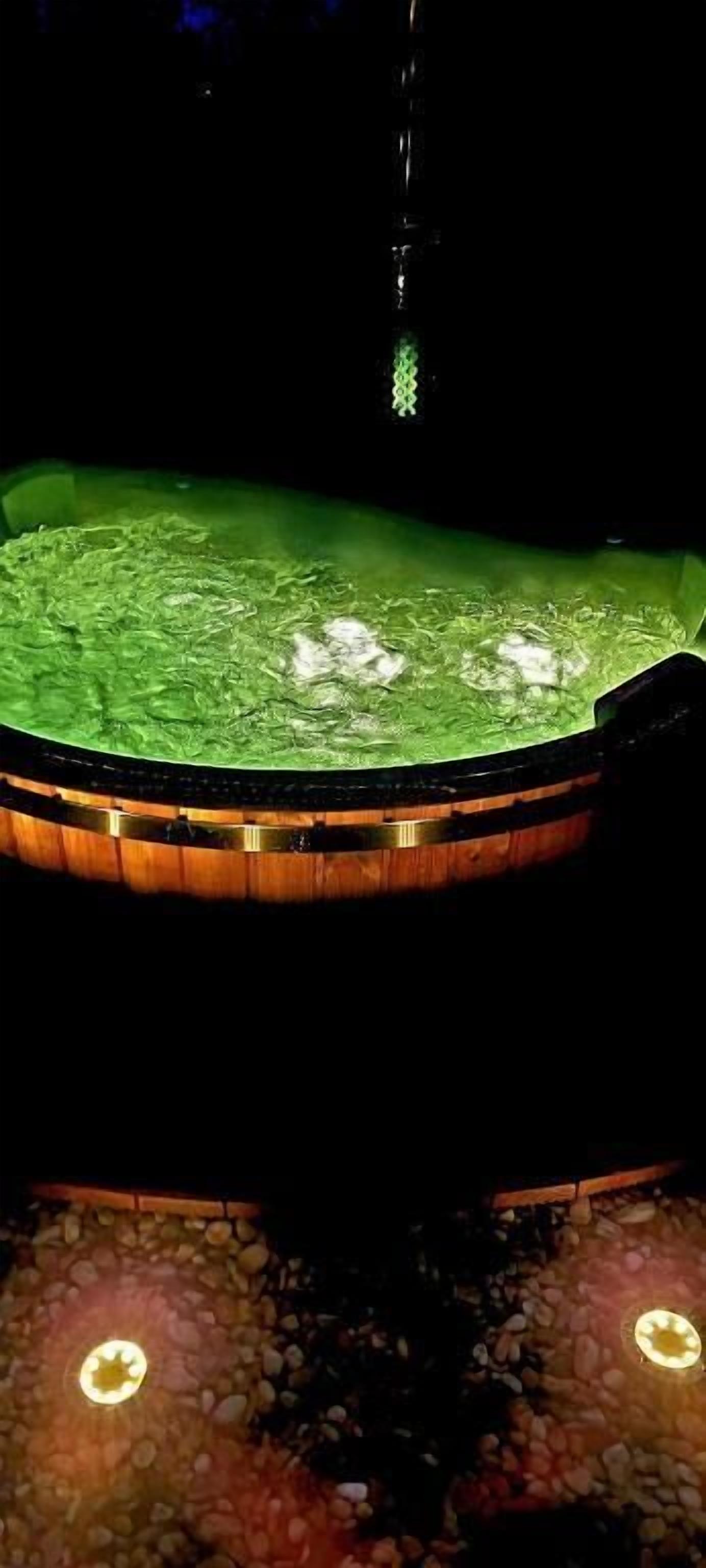 A hot tub with a wooden exterior and a green interior, surrounded by a pebble-textured floor.