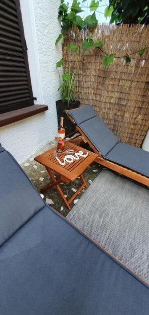Ein kleiner Sitzbereich im Freien mit zwei Liegestühlen, einem kleinen Tisch, einer Spirituosenflasche und einem Blumentopf.