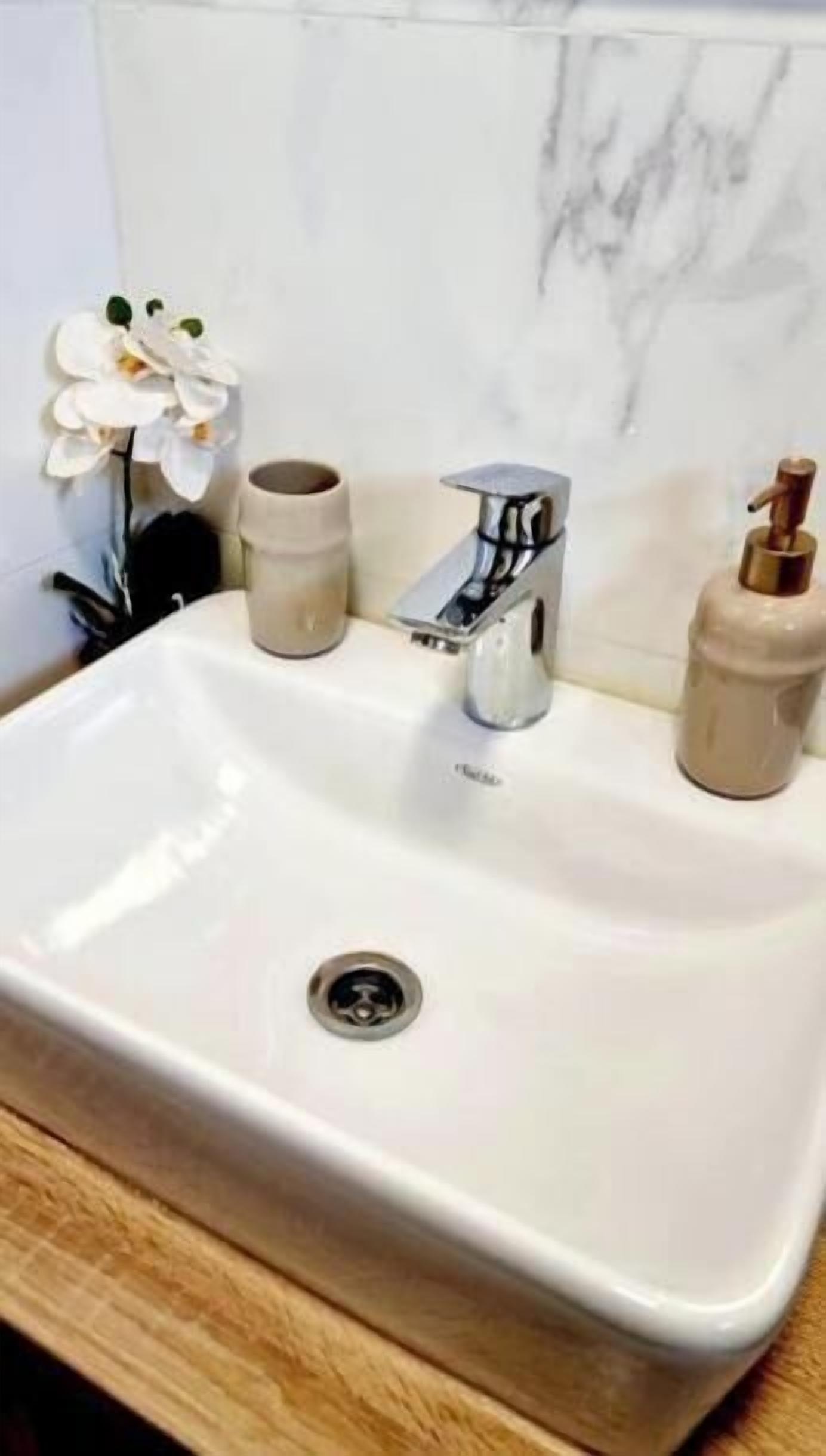 Ein Badezimmerwaschbecken mit einem modernen Wasserhahn, einer Marmorablage und einer kleinen Orchidee.