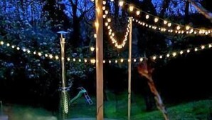 Uma área externa circular com uma fonte central, cercada por um caminho pavimentado e iluminada por luzes de cordão.