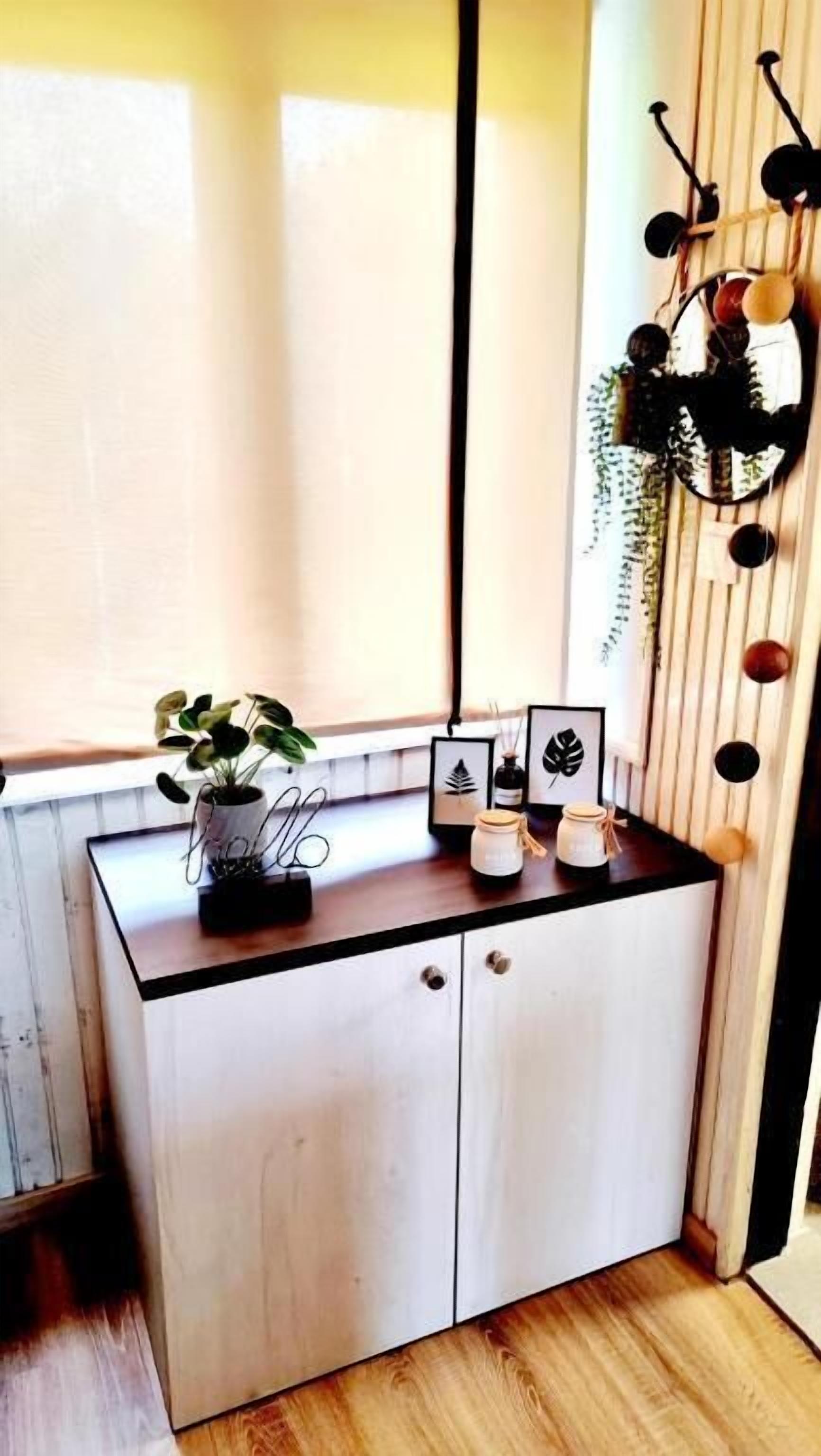 A small, white wooden cabinet with a black countertop, a potted plant, and framed pictures.