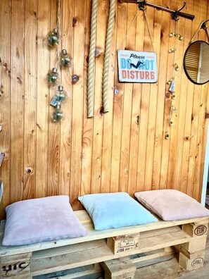 Pared de madera con un letrero que dice 'Por favor, no molestar', un banco con cojines y una cuerda colgante.