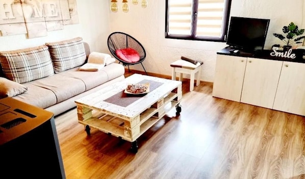A cozy living room with a sofa, a wooden coffee table, a black chair, a television on a cabinet, and a window with blinds. - Holiday House Malia Spa Hot Tub Jacuzzijem Free Entry to all City Attractions (Durdevac)