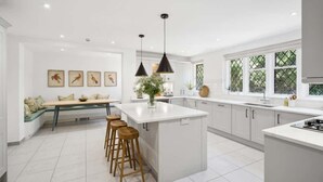 Una cocina moderna con una isla central, taburetes de bar, iluminación colgante y un comedor con banco.