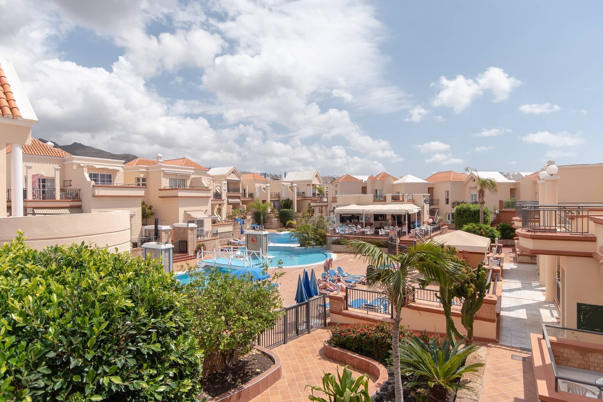 A resort with multiple buildings, a swimming pool, and a landscaped area with palm trees.
