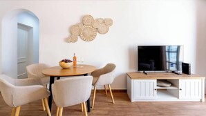 Un soggiorno moderno con un tavolo rotondo in legno, quattro poltrone imbottite, un televisore a schermo piatto su un mobile bianco e decorazioni murali.