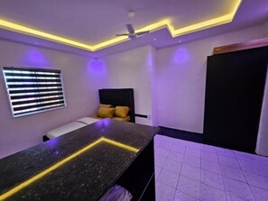 Um quarto com cama, escrivaninha, ventilador de teto e janela com persianas.