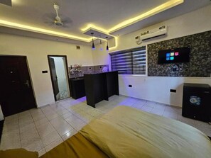 Ein Schlafzimmer mit einem Bett, einer kleinen Küchenzeile, einem Deckenventilator und einem an der Wand montierten Fernseher.