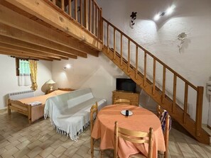A cozy room with a wooden staircase, a bed, a sofa, a table with chairs, and a television. - Spacious Studio in Castellane (Castellane)