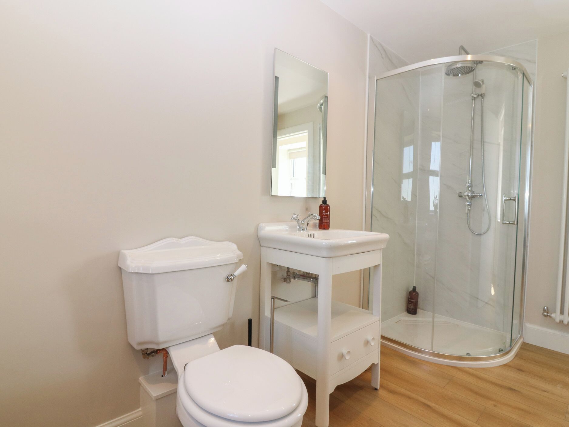Un baño con inodoro, lavabo, espejo y ducha con mampara de vidrio.
