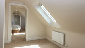A bedroom with a sloped ceiling, a skylight, a radiator, and a carpeted floor. - Shepherds Cottage (Haddington)