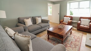 A living room with a grey sofa set, a wooden coffee table, a patterned rug, and leather armchairs.