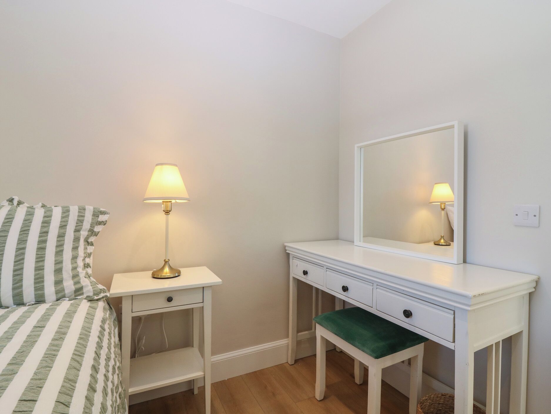 Une chambre à coucher comprenant un lit, une table de chevet avec une lampe, une commode avec un miroir et un banc.
