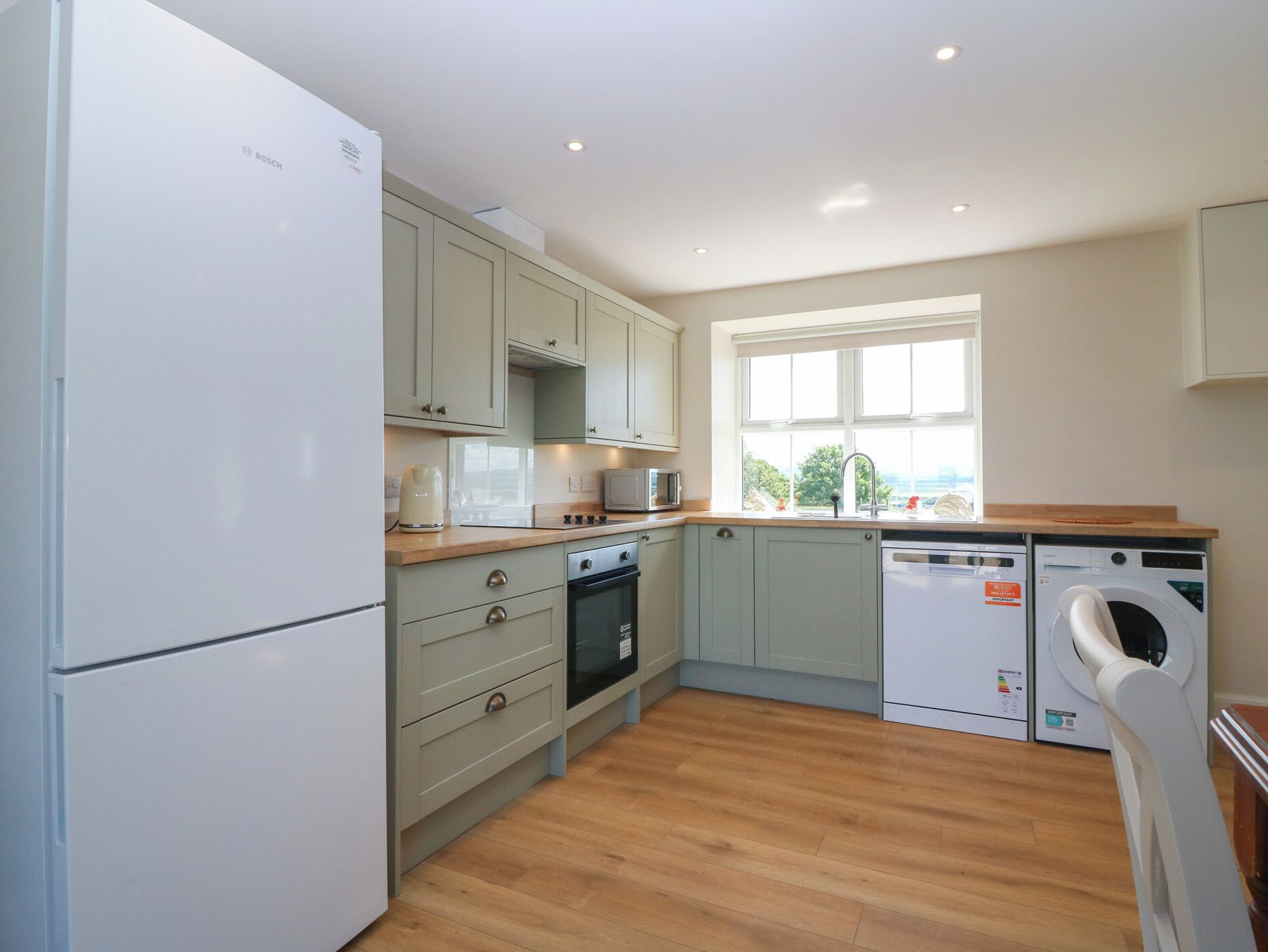 A kitchen with a refrigerator, oven, microwave, sink, and washing machine.