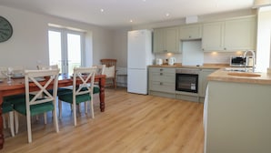 A kitchen with wooden flooring, a dining table with chairs, a refrigerator, a microwave, and cabinets.