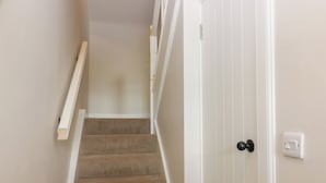 A staircase with carpeted steps leading to a door with a black handle and a light switch.