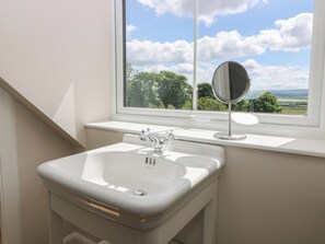 Ein Badezimmer mit einem weißen Waschbecken, einem Spiegel und einem Fenster mit Blick auf Bäume und Hügel.