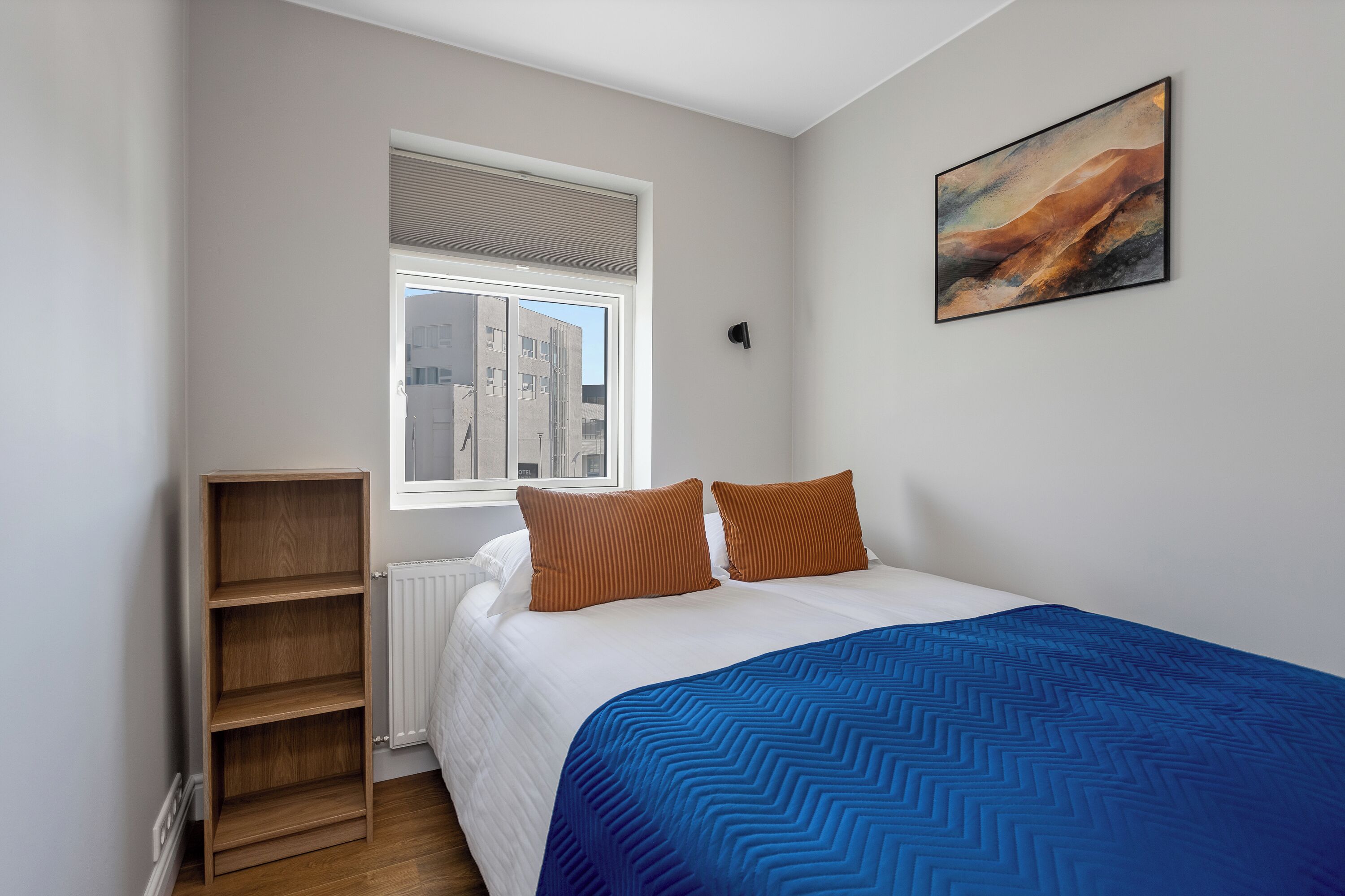 Un dormitorio con cama, ventana, radiador y un cuadro colgado en la pared.