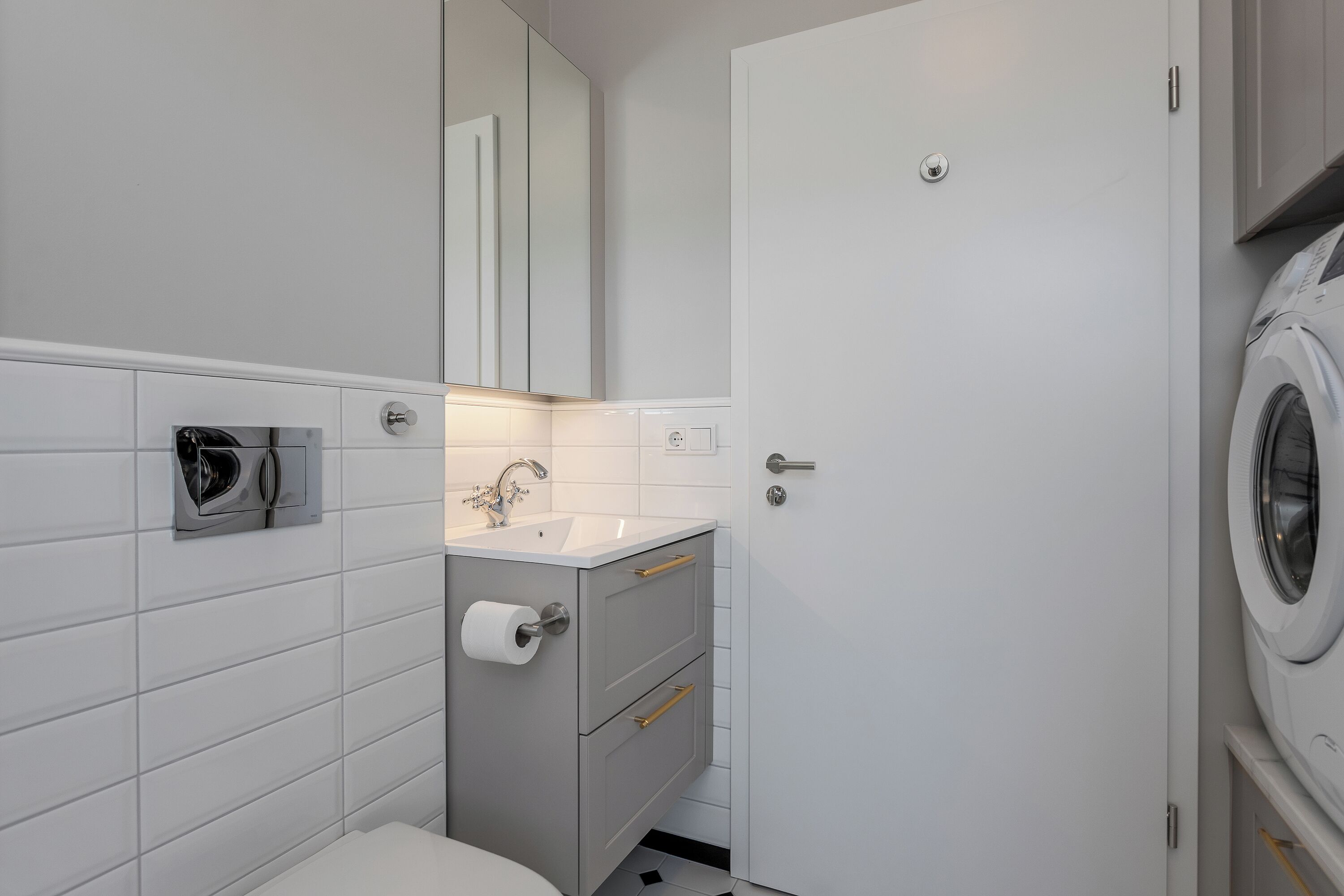 A compact bathroom with a toilet, sink, mirror, and a washing machine.