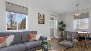 A modern living room with a grey sofa, a wooden dining table, a grey armchair, and a large window. - Aska Selfoss (Selfoss)