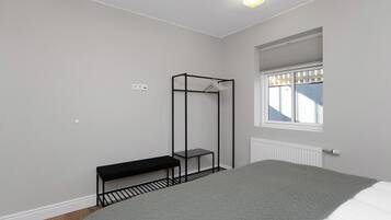 A bedroom with a bed, a bench, a metal shelf, a radiator, and a window.