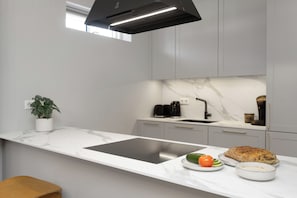 A modern kitchen with a white marble countertop, a built-in stove, a sink, and a potted plant. - Aska Selfoss (Selfoss)