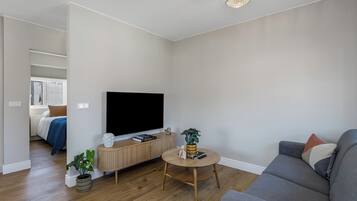 Egy modern nappali, melyben egy síkképernyős televízió, egy szürke kanapé, egy kerek dohányasztal és egy fa szekrény található.