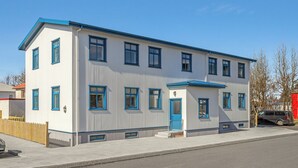 Un edificio de dos pisos con puerta y ventanas azules, un pequeño porche y un patio cercado.