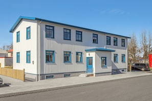 A two-story building with a blue door and windows, a small porch, and a fenced yard. - Aska Selfoss (Selfoss)