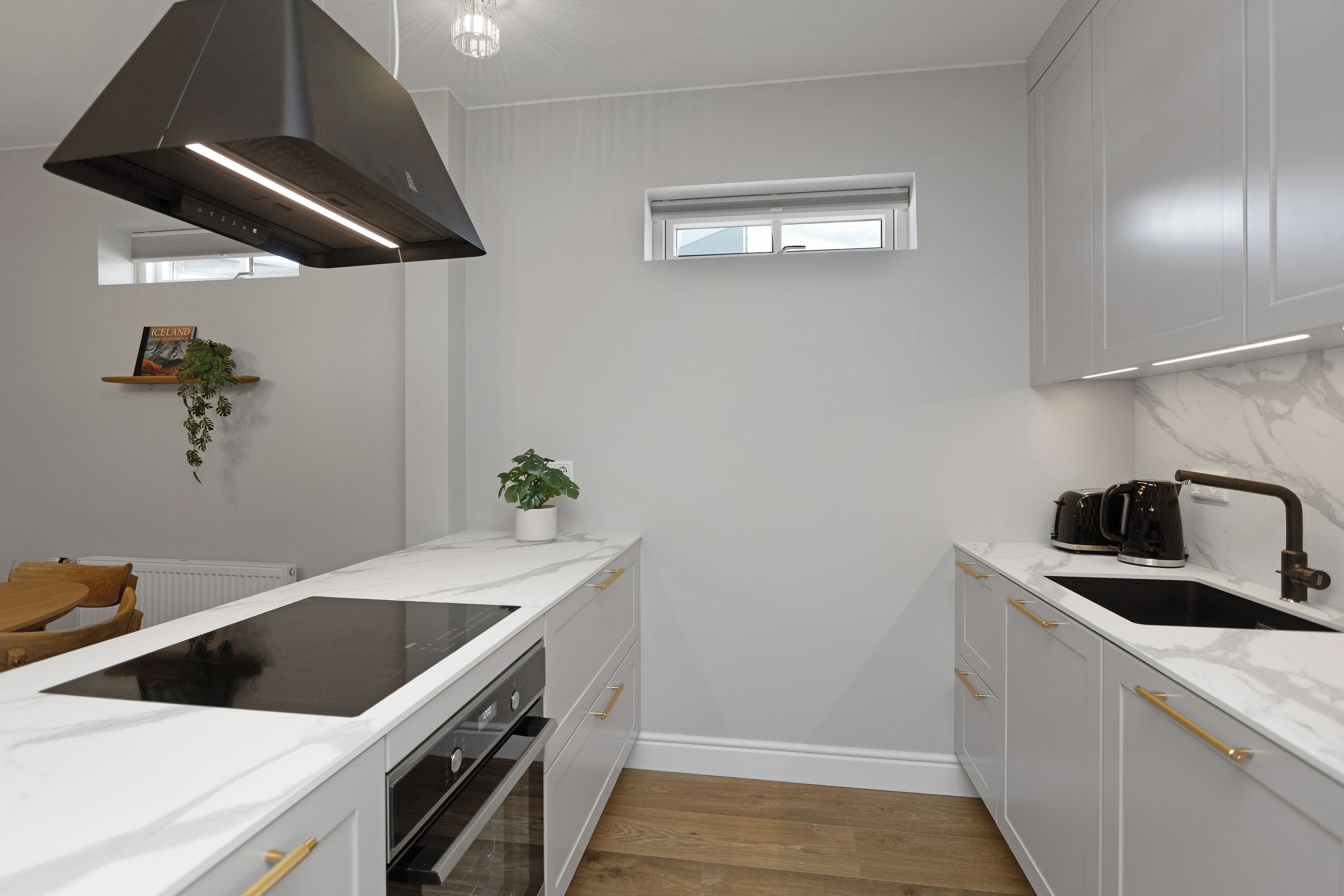 A modern kitchen with white cabinetry, a black range hood, a built-in oven, and a window above the sink.