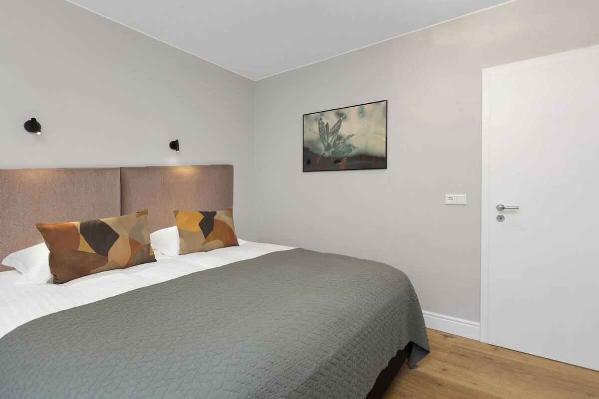 Quarto com cama, travesseiros, cabeceira, um quadro e uma porta.