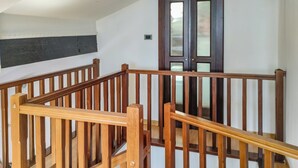 Een houten trap met een leuning, een donkerhouten deur met ruitpanelen, en een witte muur met een donkere horizontale strook.