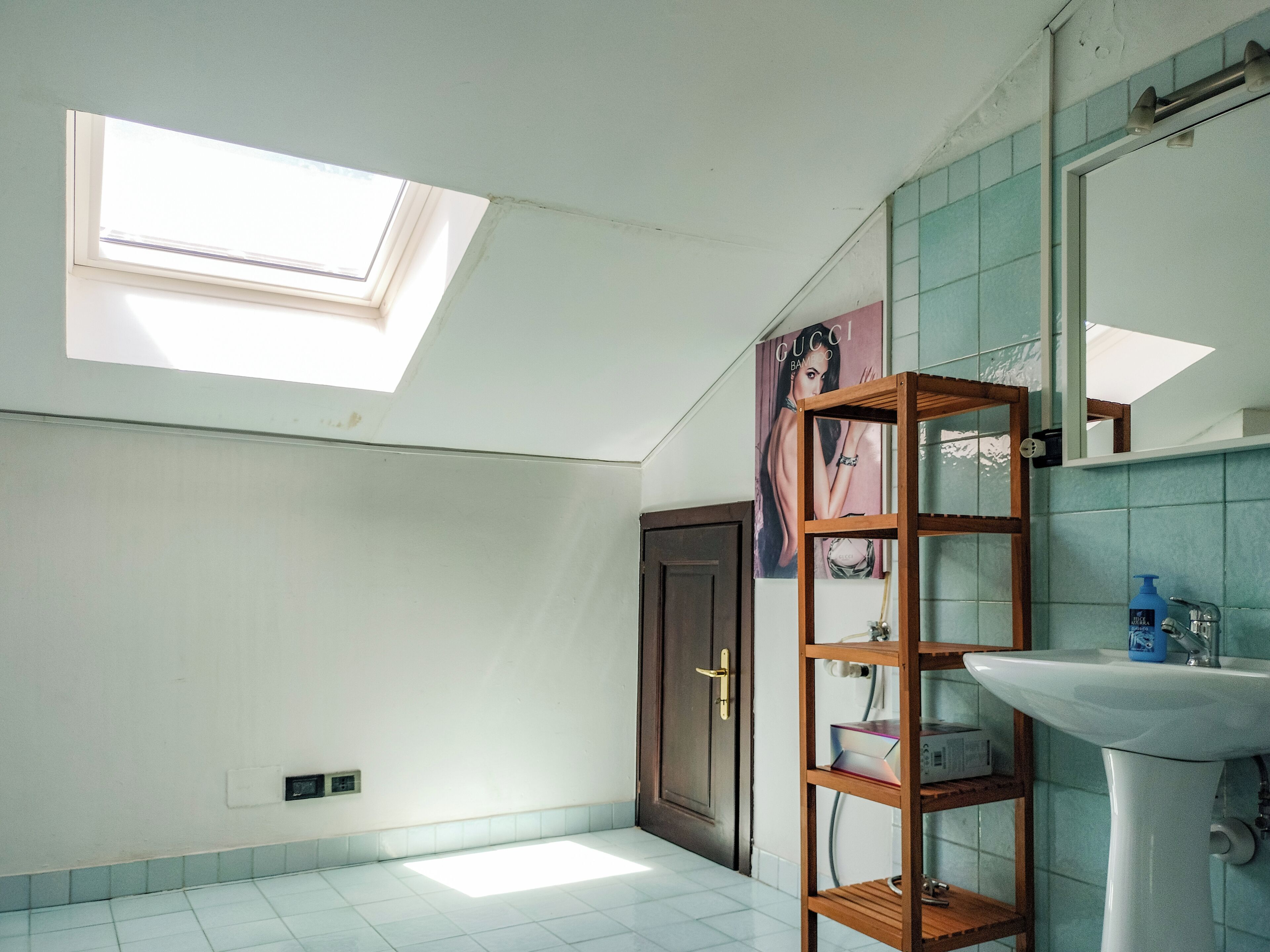 Une salle de bain avec un puits de lumière, une étagère en bois, un lavabo blanc et un miroir.