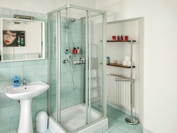 A bathroom with a glass-enclosed shower, a pedestal sink, and a mirror above it.